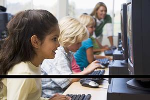 Children at computer terminals with teacher in background (depth of field/high key)