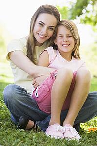 Woman and young girl outdoors embracing and smiling
