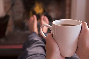 Feet warming at fireplace with hands holding coffee