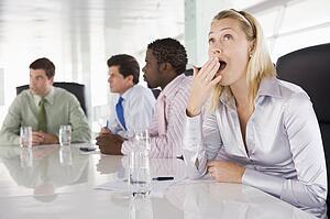 Four businesspeople in boardroom with one businesswoman yawning