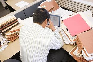 Businessman in cubicle with laptop and stacks of files
