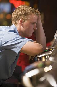 Man in casino playing slot machine frustrated with people in background (selective focus)