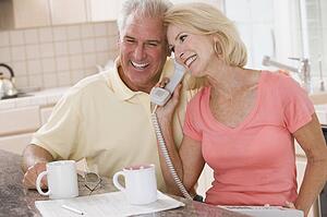 Couple in kitchen with coffee using telephone together and smiling