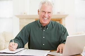 Man in dining room with laptop and paperwork smiling