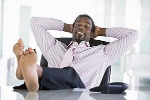 Businessman sitting in office with feet on desk relaxing and smiling