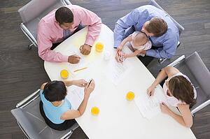 Four businesspeople in boardroom with one holding a baby