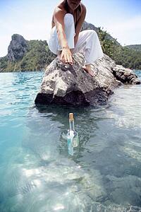 Woman outdoors reaching into ocean for bottle with note inside (selective focus)
