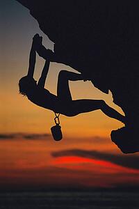 Mountain climber coming up under mountain cliff (silhouette)