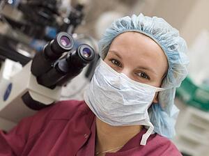 Embryologist sitting by microscope with mask on (selective focus)