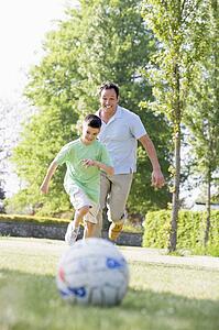 Man and young boy outdoors playing soccer and having fun