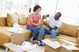 Couple relaxing with champagne by boxes in new home smiling