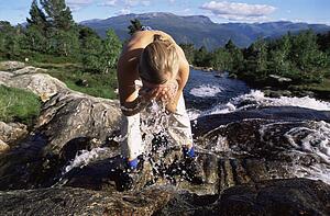 Woman outdoors by river splashing water on face (selective focus)