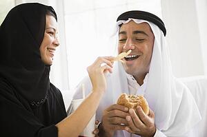 Couple eating fast food in living room and smiling (high key/selective focus)