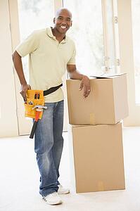 Man wearing tool belt standing by boxes in new home smiling