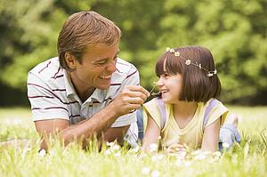 Father and daughter lying outdoors with flowers smiling