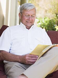 Senior woman sitting outdoors on a chair reading a book
