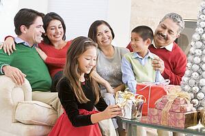 Family Sitting On Sofa In Front Of Christmas Presents, Young Girl Selecting A Gift