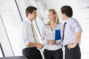 Three businesspeople standing in corridor talking and smiling