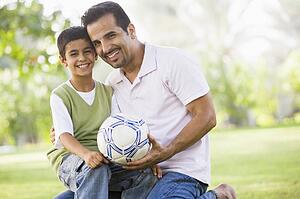 Father and son outdoors in park with ball smiling (selective focus)