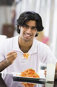Man at restaurant eating spaghetti and smiling (selective focus)