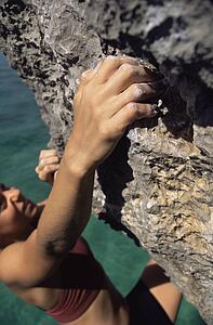 Woman climbing rocks in swimwear by ocean (selective focus)