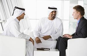 Three businessmen indoors with a laptop talking and smiling (high key/selective focus)