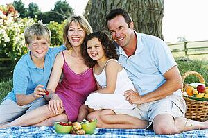 Family sitting outdoors with picnic smiling
