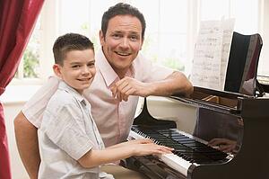 Man and young boy playing piano and smiling