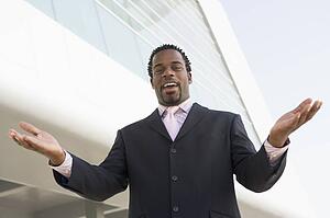 Businessman standing outdoors by building with hands out smiling