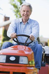 Man outdoors driving lawnmower smiling