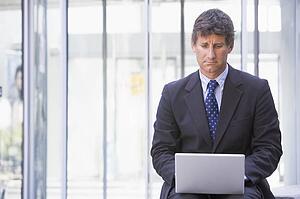 Businessman sitting in office lobby using laptop