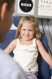 Optometrist in exam room with young girl in chair smiling
