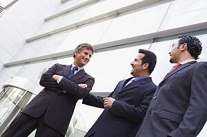 Three businessmen standing outdoors by building talking and smiling (high key/selective focus)