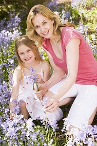 Mother and daughter outdoors holding flowers smiling