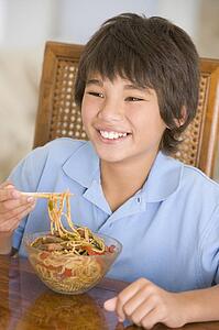 Young boy in dining room eating chinese food smiling