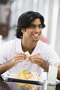 Man at restaurant eating sandwich and smiling (selective focus)