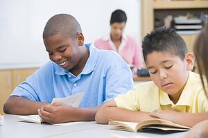 Students in class reading with teacher in background (selective focus)