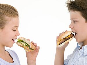 Sister eating sandwich by brother eating cheeseburger