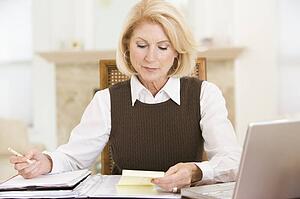 Woman in dining room with laptop and paperwork