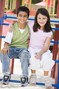 Two young children sitting on playground structure smiling (selective focus)