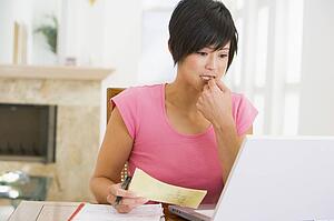 Woman in dining room with laptop thinking