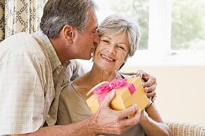 Husband giving wife gift in living room kissing her and smiling