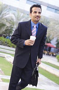 Businessman walking outdoors with coffee smiling (high key/selective focus)