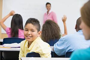 Student in class looking at camera with teacher in background (selective focus)