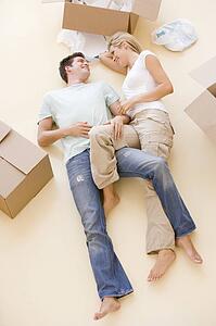Couple lying on floor by open boxes in new home smiling
