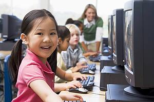 Children at computer terminals with teacher in background (depth of field/high key)