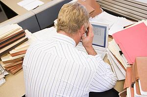 Businessman in cubicle with laptop and stacks of files