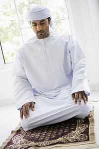 Man in turban praying on mat (high key)