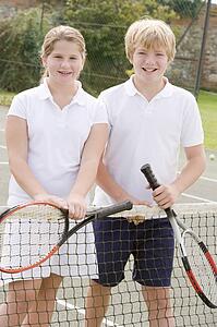 Two young friends with rackets on tennis court smiling