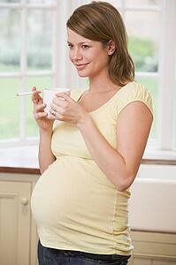 Pregnant woman standing in kitchen with coffee and cigarette smiling